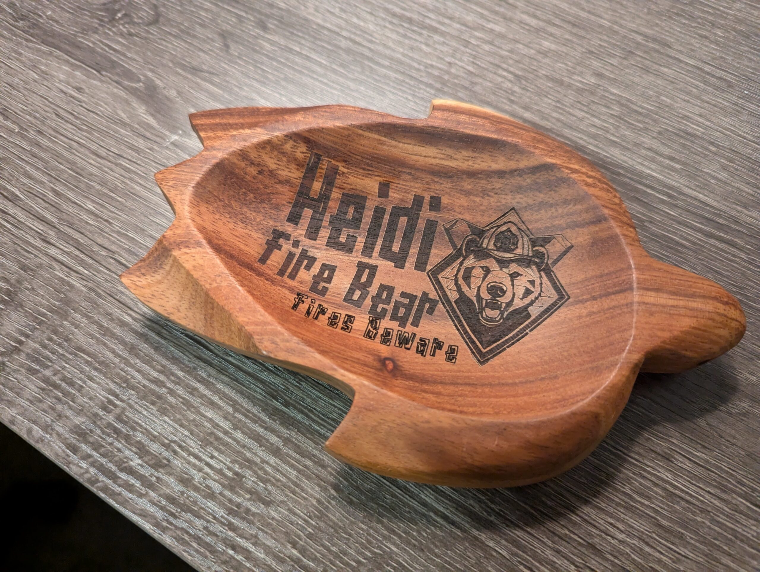 一个乌龟造型的硬木托盘的斜角视图,上面雕刻着「Heidi Fire Bear — Fires Beware」字样和一个几何风格的熊徽章
